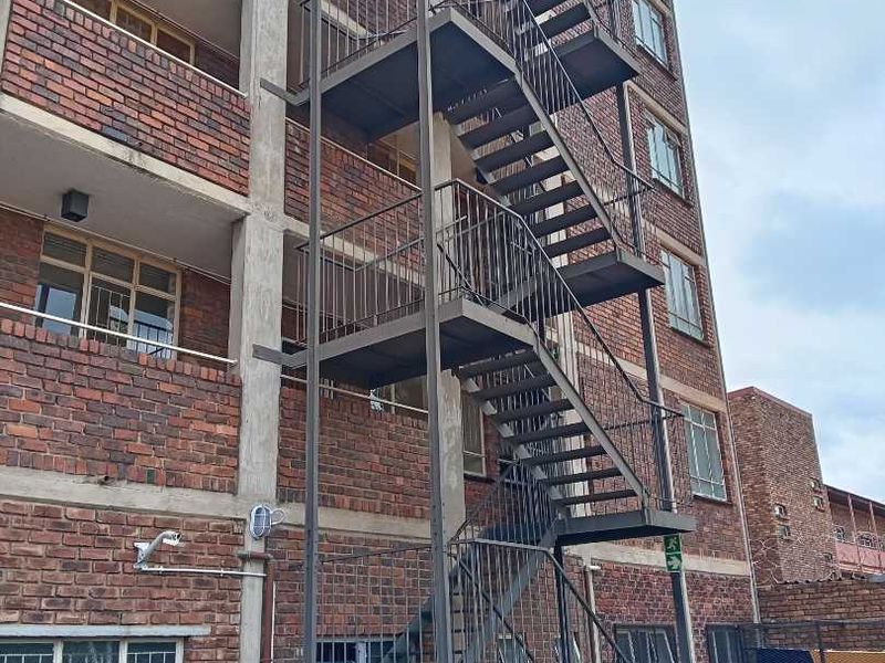 Exterior view of an apartment building featuring a multi-level steel fire escape staircase and traditional face brick facade.