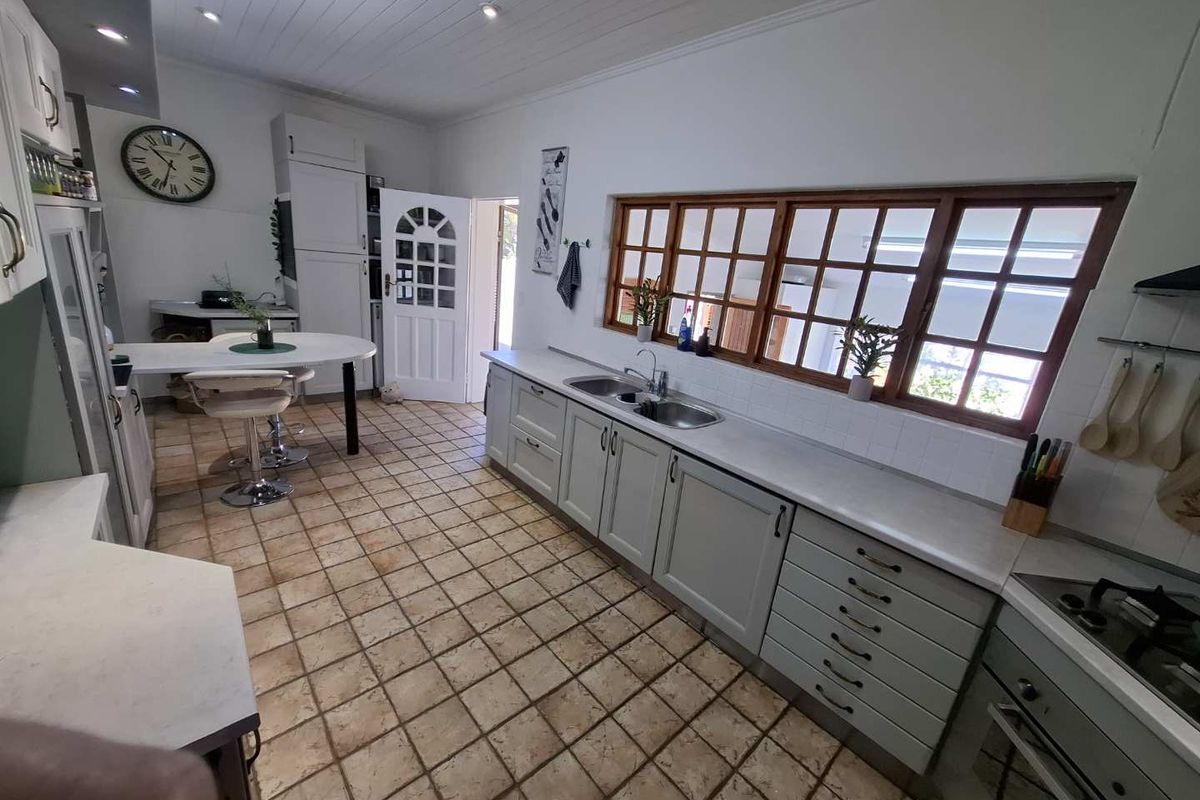 A functional kitchen featuring light-toned cabinetry, a double basin sink, built-in oven, and classic tiled flooring with timber-framed windows.