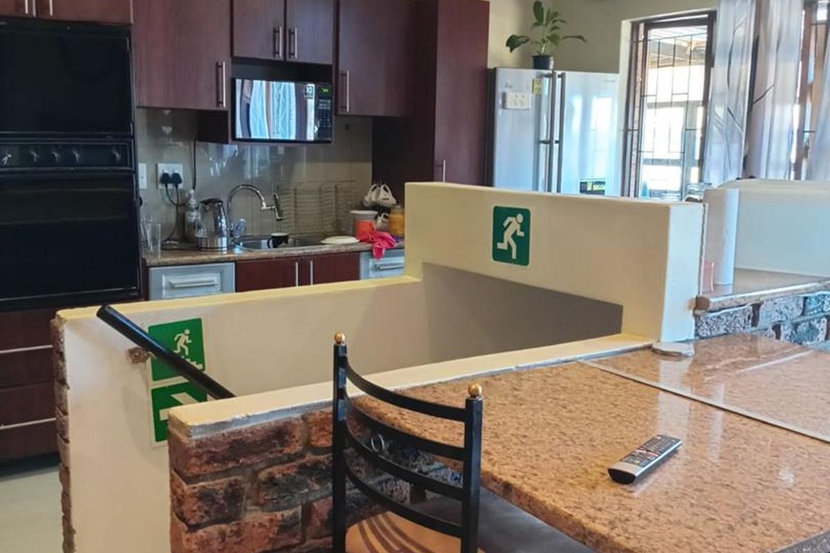 A kitchen area featuring dark wood cabinetry, built-in oven, and a breakfast bar with granite countertop, adjacent to a staircase with safety signage.
