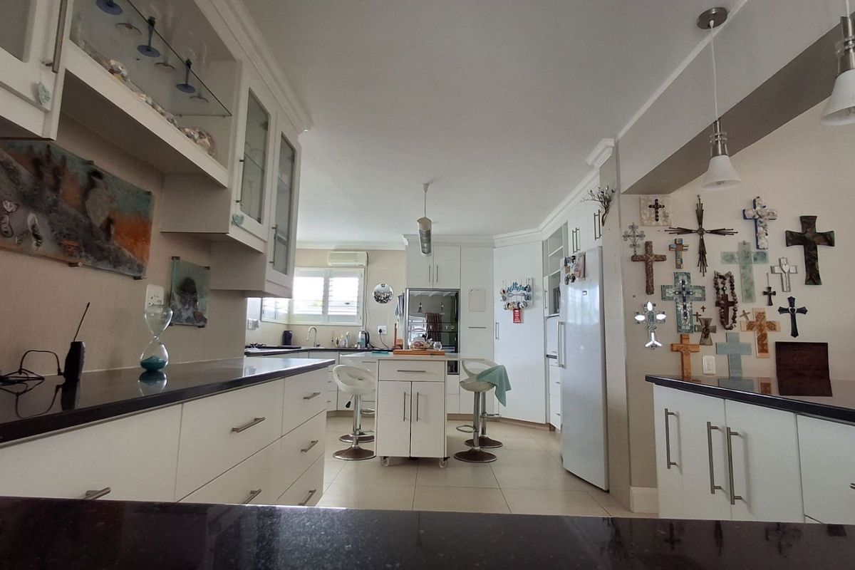 A spacious kitchen featuring white cabinetry, dark granite countertops, tiled flooring, and modern pendant lighting, offering a functional and well-lit culinary workspace.