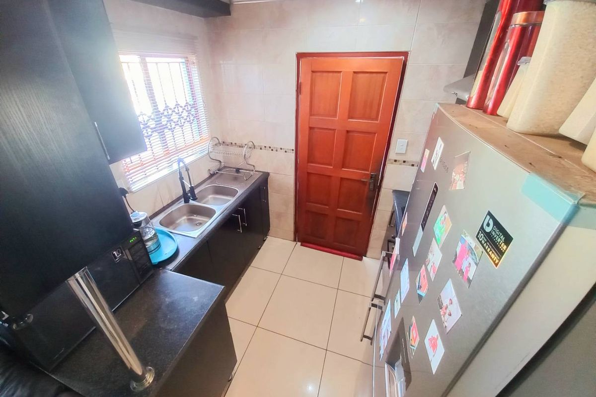 A compact kitchen featuring dark cabinetry, a double stainless steel sink, tiled walls, and tiled flooring with direct access to an exterior door.