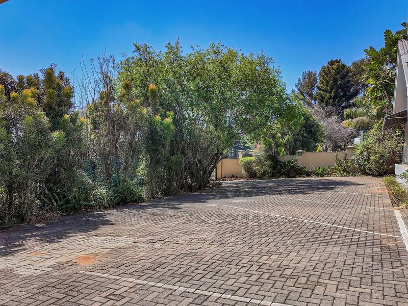 A spacious paved driveway area leading to the front entrance of the house, featuring established garden borders and a secure boundary wall.