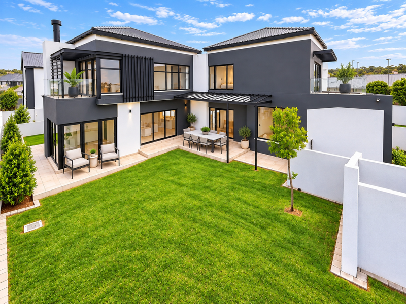 Modern double-story residence featuring a spacious rear garden, tiled patio area with pergola, and large sliding glass doors for seamless indoor-outdoor living.
