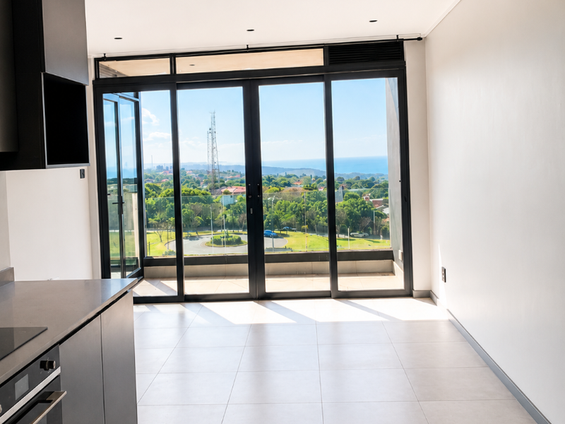 Modern open-plan kitchen and living area featuring sleek dark cabinetry, integrated appliances, large glass sliding doors, and expansive views.