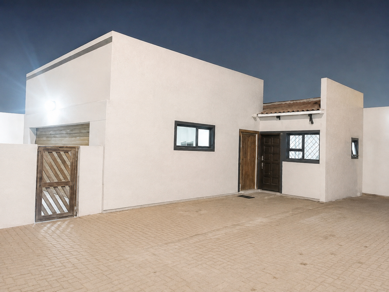 Modern exterior front facade featuring a paved driveway, secure wooden pedestrian gate, and clean white rendered walls with dark aluminium window frames.
