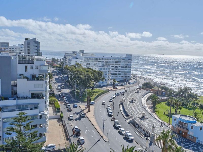 Elevated panoramic view overlooking the coastal road, urban apartment buildings, and the oceanfront promenade.