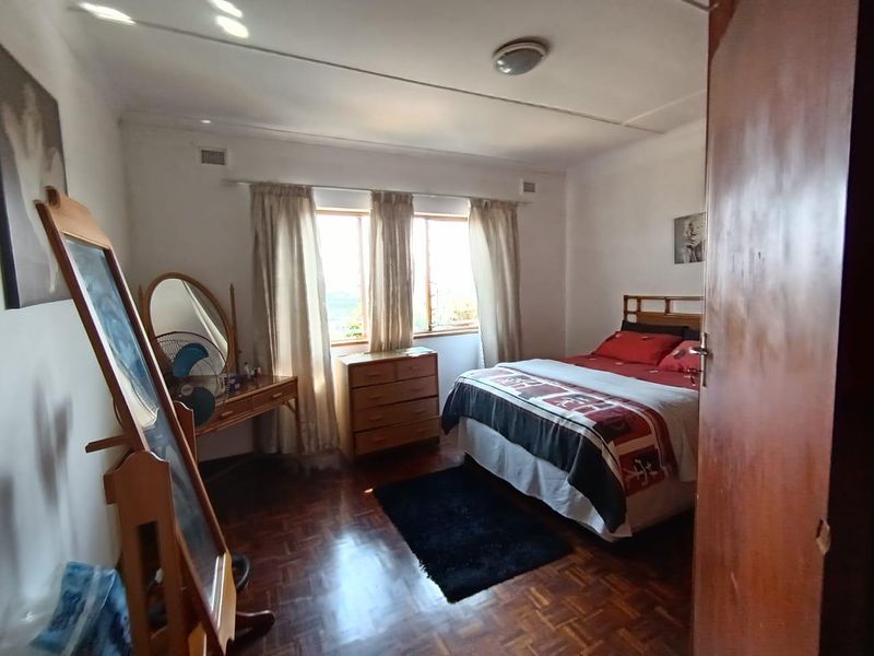 A bedroom featuring parquet flooring, a central ceiling light, and a window allowing natural light.