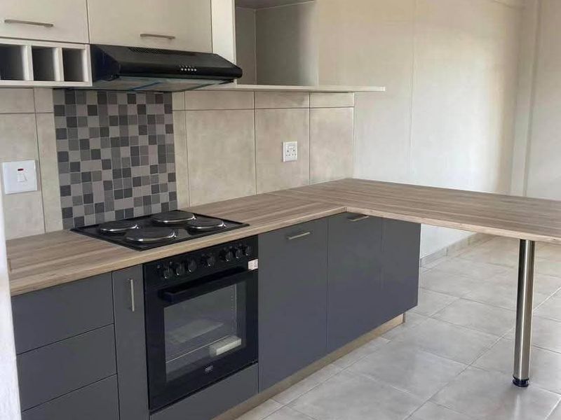 Modern kitchen featuring dark grey base cabinets, light upper cabinetry, wood-look laminate countertops, integrated oven, hob, and a convenient breakfast bar extension.