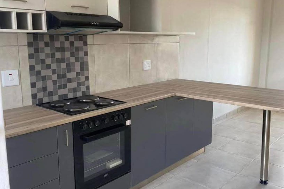 Modern kitchen featuring dark grey base cabinets, light upper cabinetry, wood-look laminate countertops, integrated oven, hob, and a convenient breakfast bar extension.