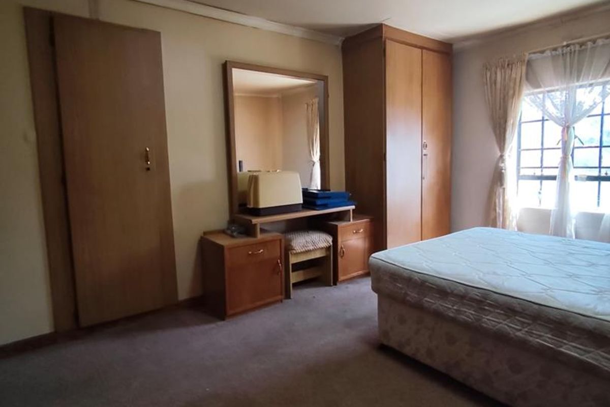 A bedroom featuring built-in cupboards, a vanity unit, and carpeted flooring. The space is dated and would benefit from modern updates.