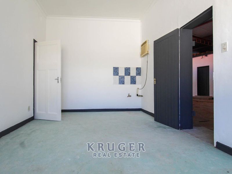 An empty utility or laundry space featuring a wall-mounted tap, plumbing connections, and a window-mounted air conditioning unit.