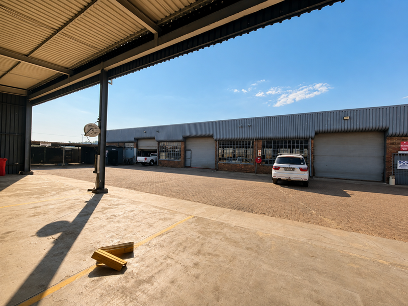 Spacious industrial yard area featuring a covered loading bay, paved driveway, and multiple roller shutter doors providing access to the warehouse facility.