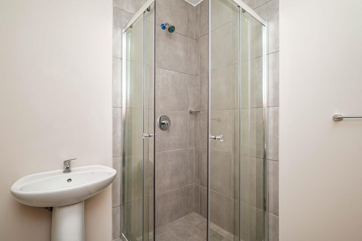A clean, modern bathroom featuring a pedestal basin and a glass-enclosed shower with neutral wall and floor tiling.