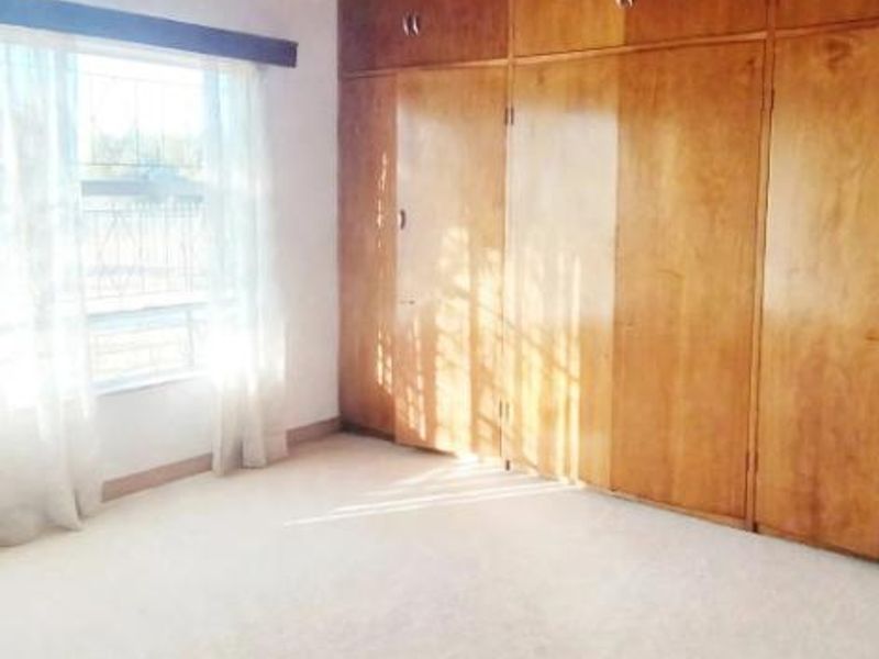 A spacious bedroom featuring a high exposed timber beam ceiling and extensive built-in wooden cabinetry, providing ample storage space.