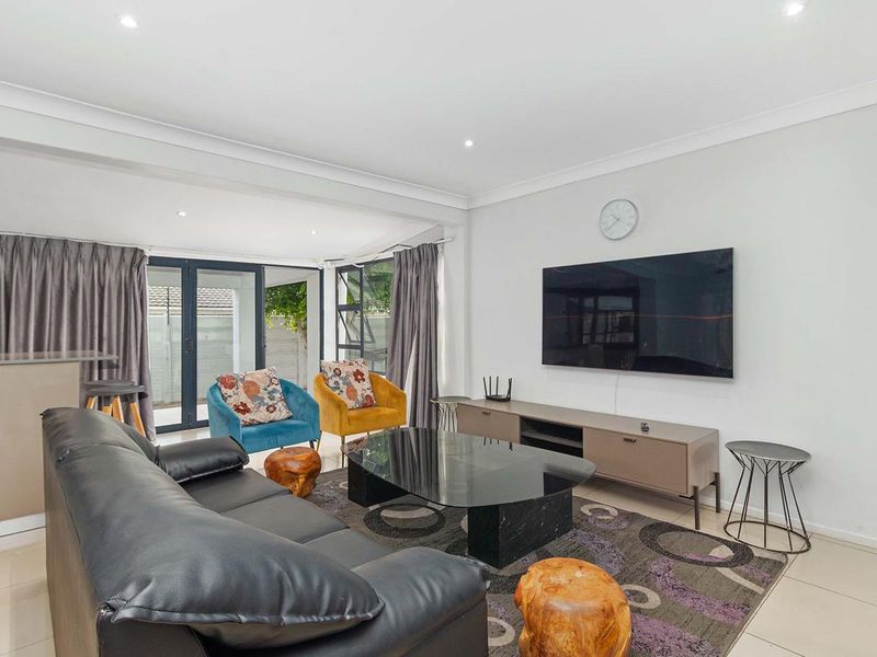 A bright and modern living room featuring tiled flooring, recessed downlighting, and large aluminium sliding doors providing access to the outdoor area.