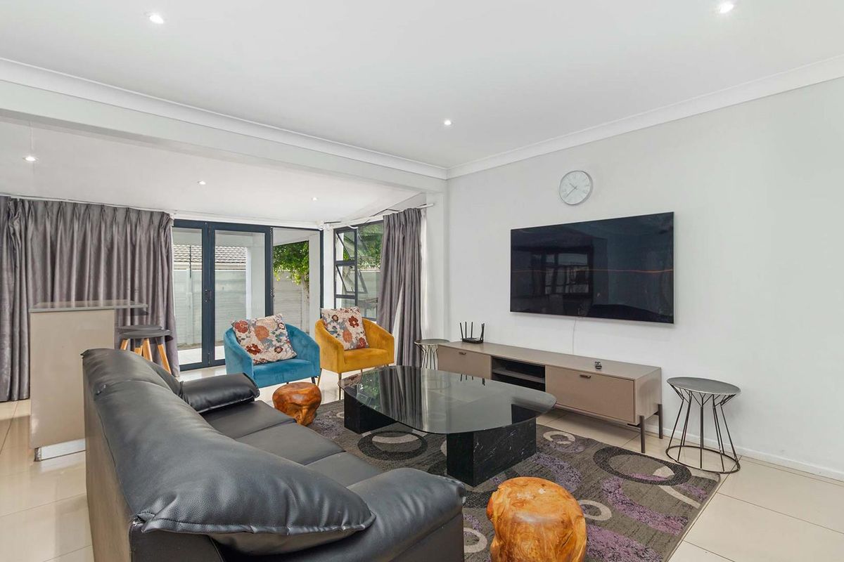 A bright and modern living room featuring tiled flooring, recessed downlighting, and large aluminium sliding doors providing access to the outdoor area.