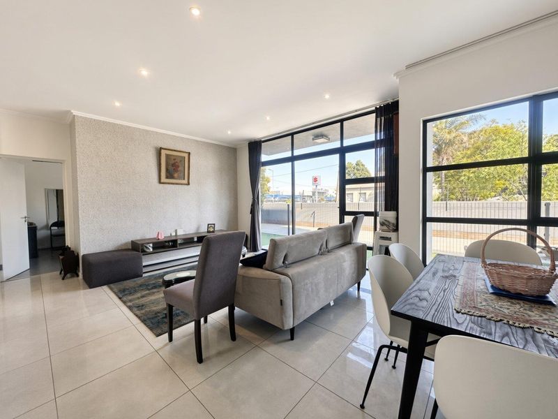 Bright open-plan living and dining area featuring large black-framed windows, neutral tiled flooring, and modern recessed downlighting.
