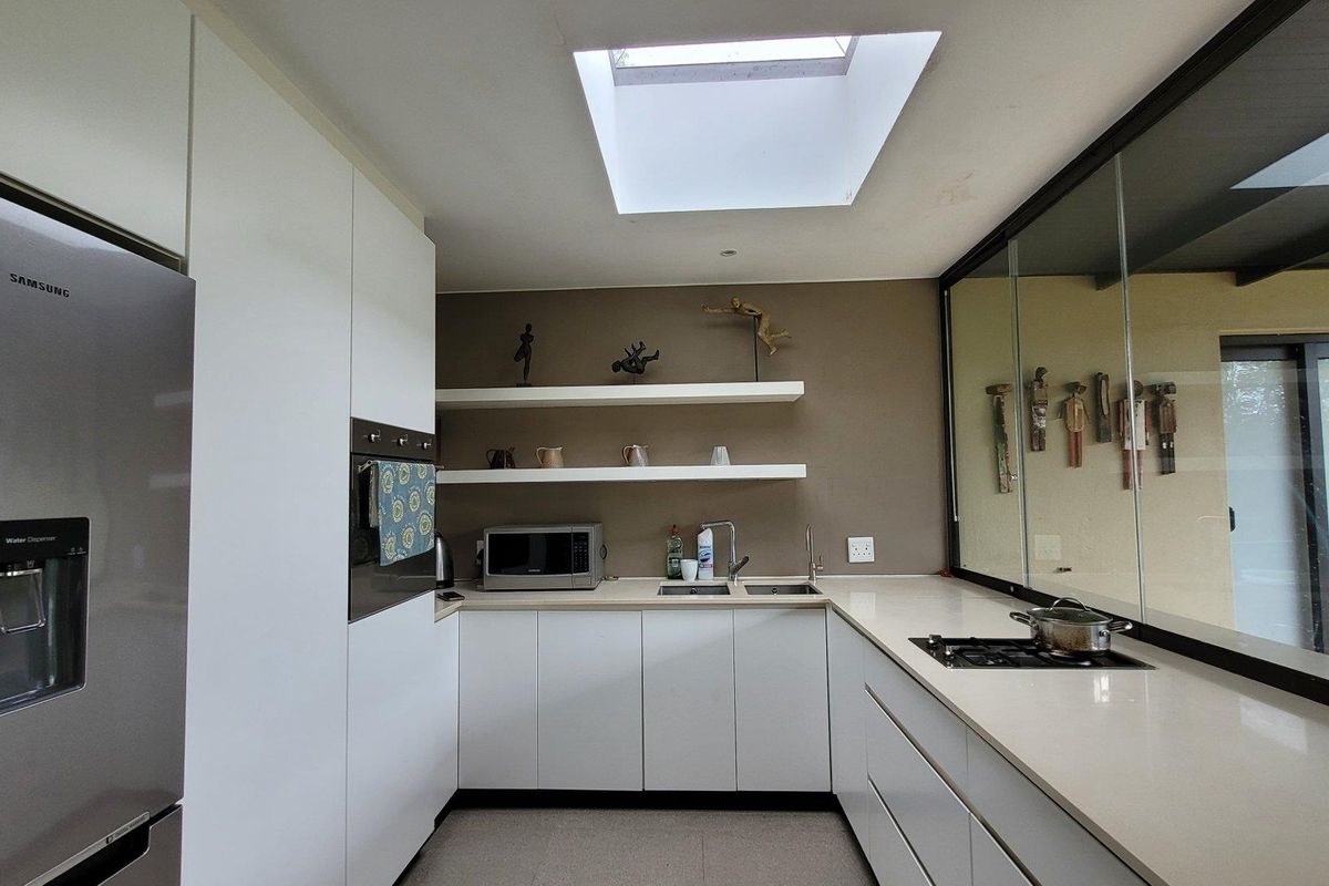 Modern kitchen featuring white cabinetry, stone countertops, integrated gas hob, built-in oven, and a skylight providing natural light.
