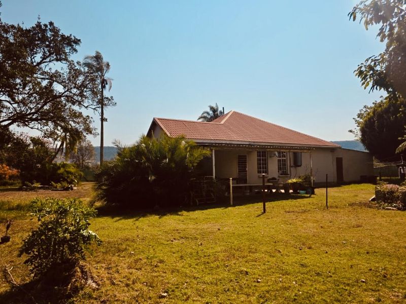 A rear view of the house featuring a tiled roof and a covered patio area overlooking a spacious garden.