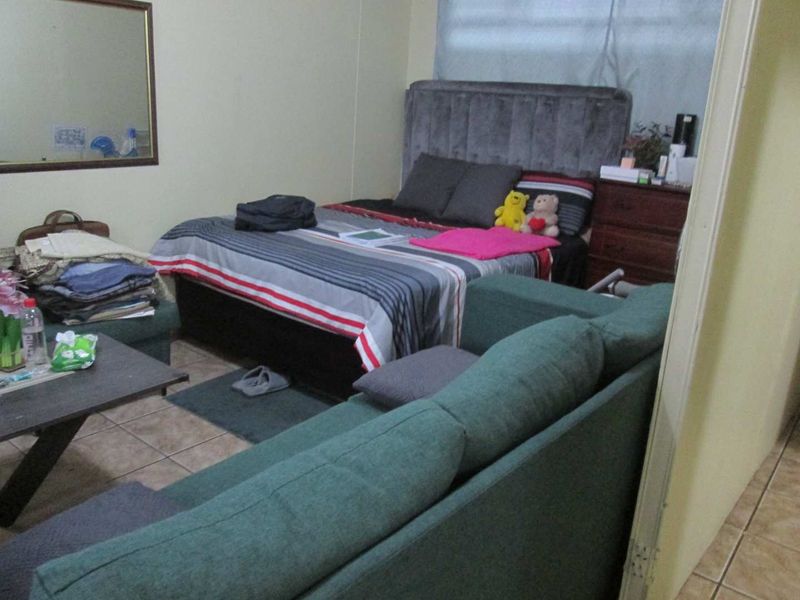 A bedroom featuring tiled flooring and a wall-mounted mirror, currently furnished with a bed and seating area.