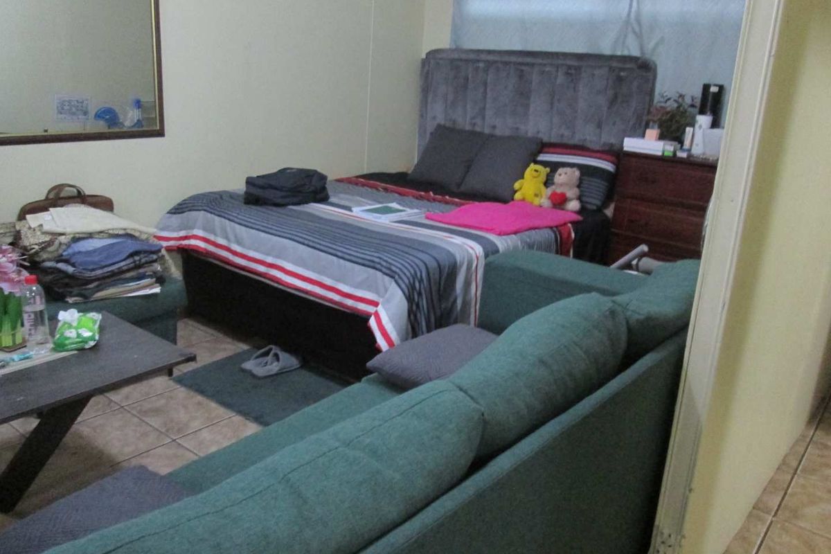 A bedroom featuring tiled flooring and a wall-mounted mirror, currently furnished with a bed and seating area.