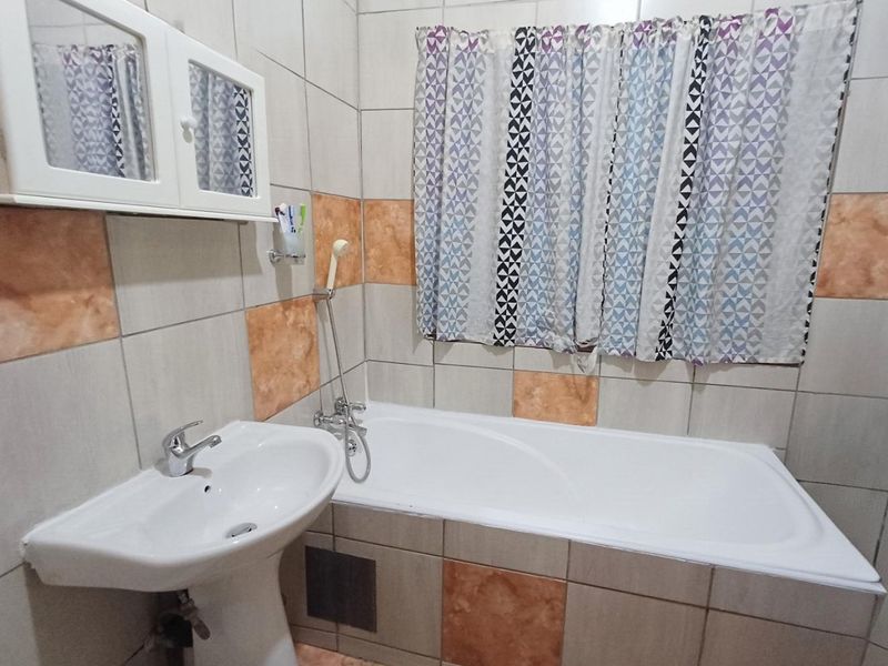 A functional bathroom featuring a pedestal basin, a bathtub with a handheld shower mixer, and tiled walls with a decorative accent band.