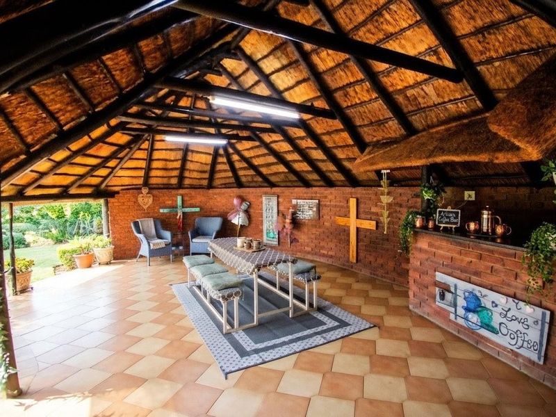 Spacious covered outdoor entertainment area featuring a traditional thatched roof, exposed timber rafters, brick walls, and a built-in brick bar counter.