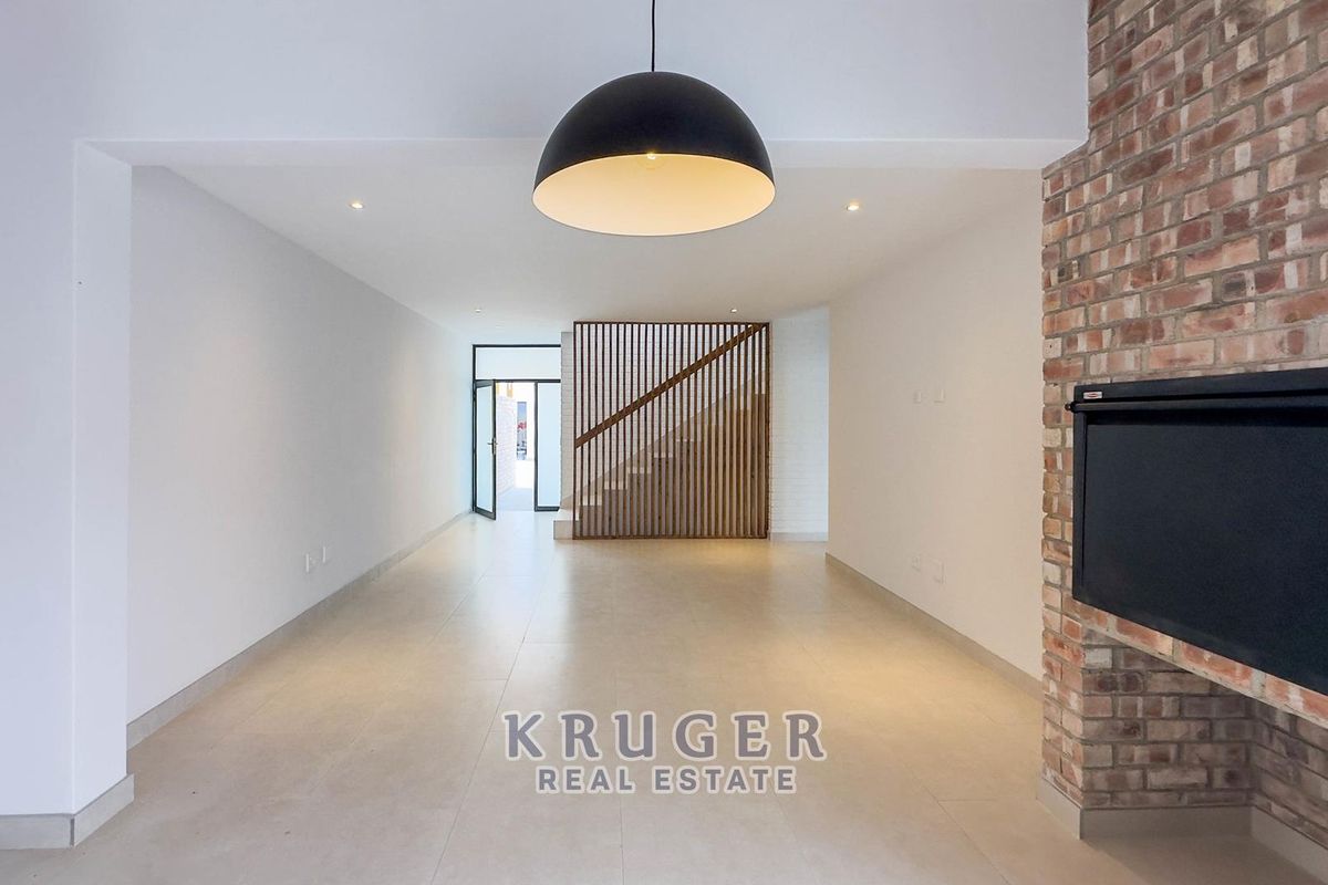 Spacious open-plan living area featuring tiled floors, an exposed brick fireplace, and a modern timber slat staircase screen.
