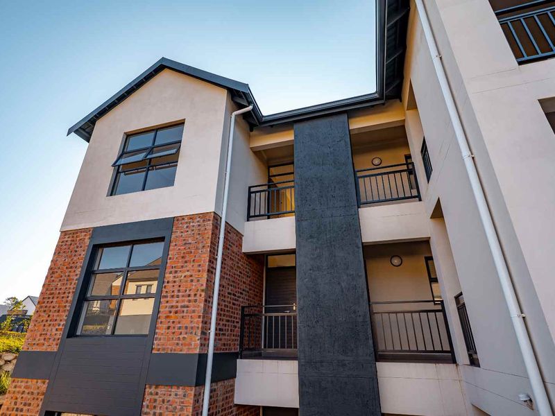 A modern apartment building exterior featuring a combination of face brick and plastered finishes with metal balcony railings and large casement windows.