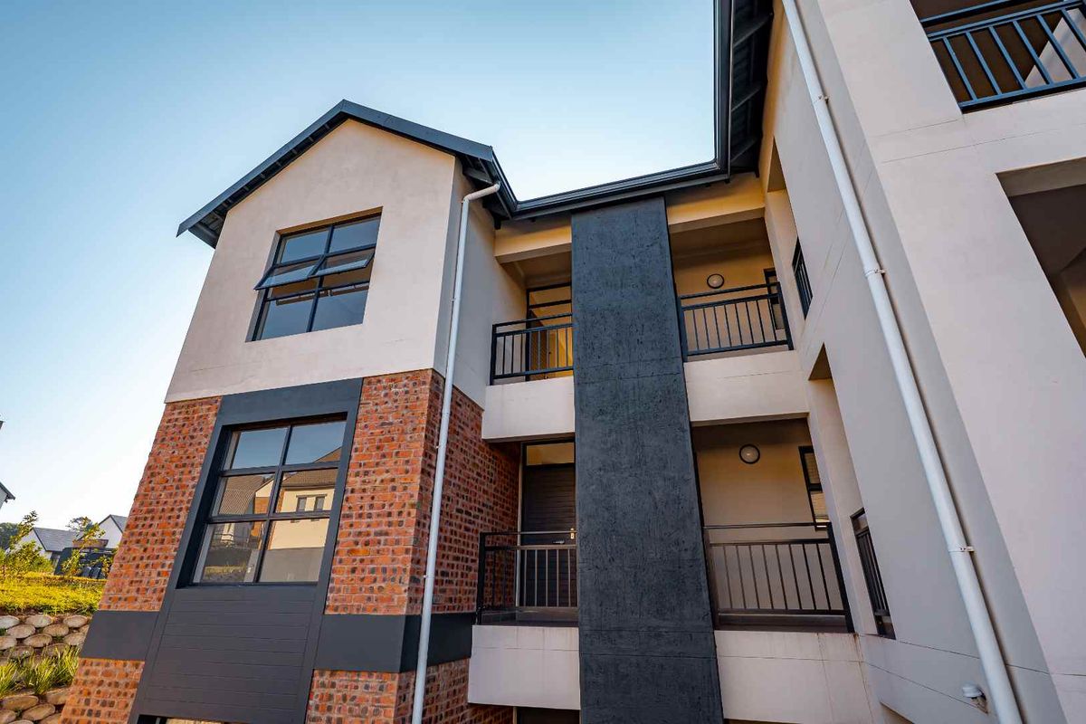 A modern apartment building exterior featuring a combination of face brick and plastered finishes with metal balcony railings and large casement windows.
