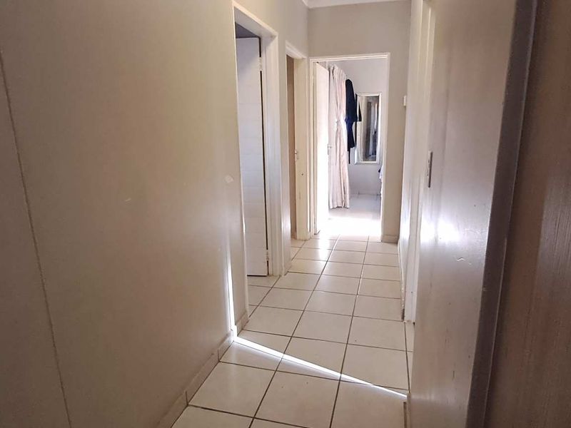 A simple, neutral-toned hallway featuring tiled flooring and access to multiple rooms within the property.