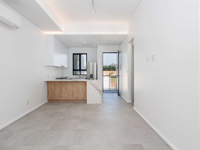 Modern open-plan kitchen and living area featuring neutral tiled floors, sleek cabinetry, stone-look countertops, and direct access to an outdoor balcony.