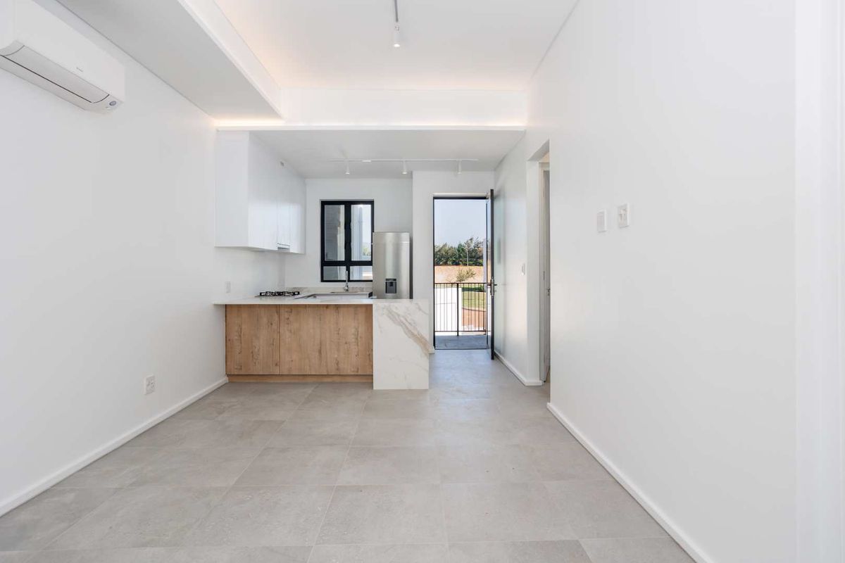 Modern open-plan kitchen and living area featuring neutral tiled floors, sleek cabinetry, stone-look countertops, and direct access to an outdoor balcony.