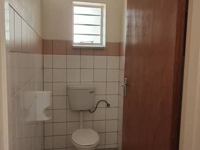 A small, functional bathroom featuring tiled walls and flooring, a standard toilet, and a louver window for ventilation.