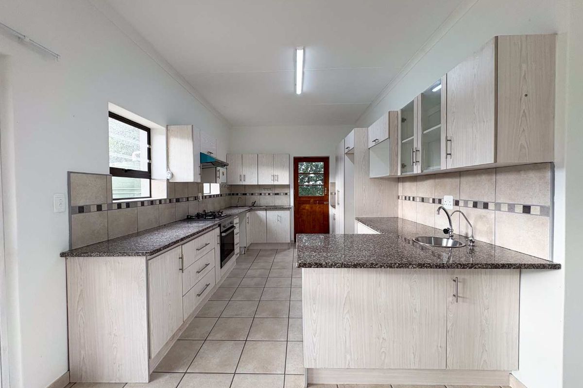 Spacious kitchen featuring light wood-grain cabinetry, granite countertops, tiled flooring, and a built-in oven and hob.