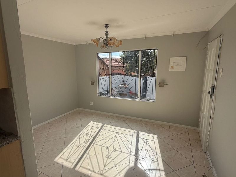 An empty living area featuring tiled flooring, a window with security bars, and a central ceiling light fixture.