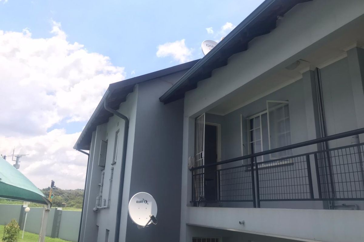 Exterior view of the apartment building featuring a balcony with metal railings, satellite dishes, and security gates on the windows.