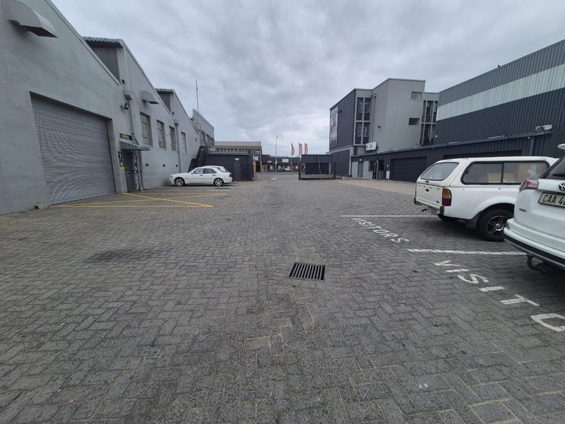 Industrial property exterior featuring a paved parking area with designated visitor bays and roller shutter access points to the warehouse units.