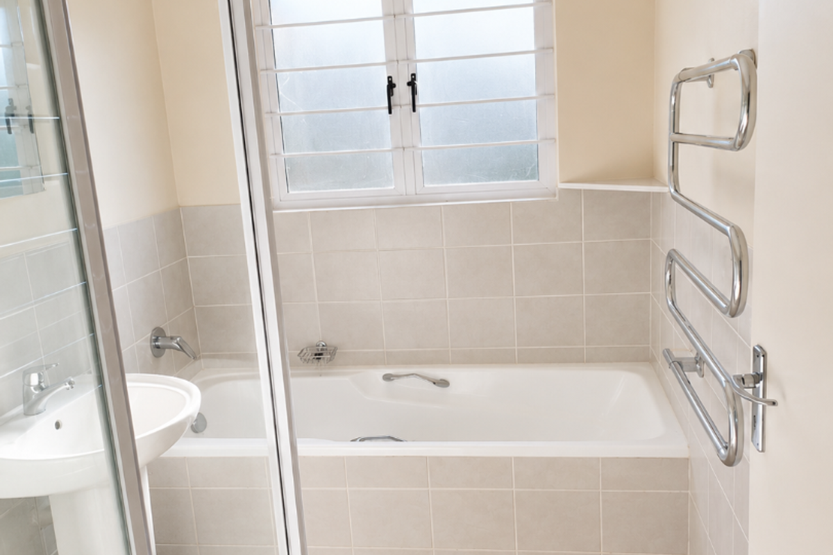 A clean, functional bathroom featuring a pedestal basin, a built-in bathtub with tiled surround, a separate shower enclosure, and a wall-mounted heated towel rail.