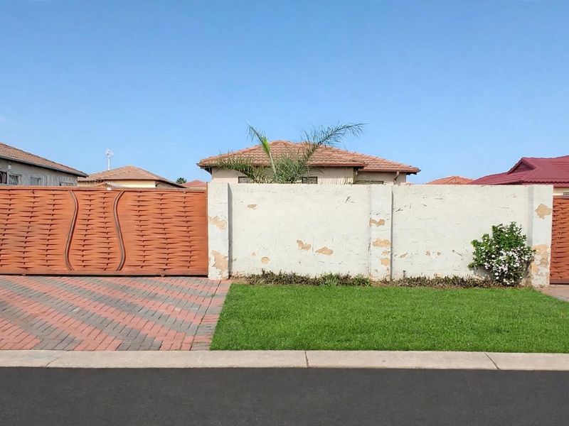 Front view of the property featuring a paved driveway, secure sliding gate, pedestrian gate, and a perimeter wall requiring maintenance and repainting.