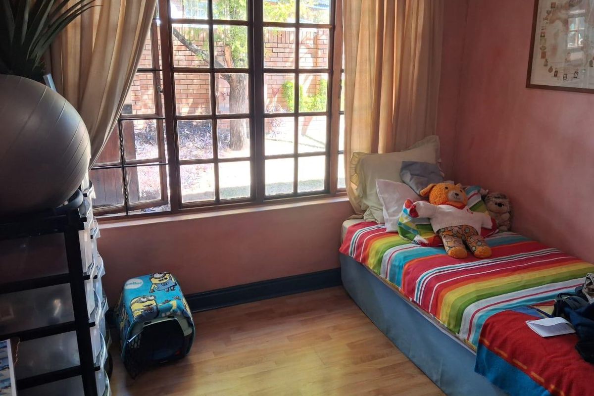 A bedroom featuring laminate flooring and a large timber-framed window overlooking the garden area.