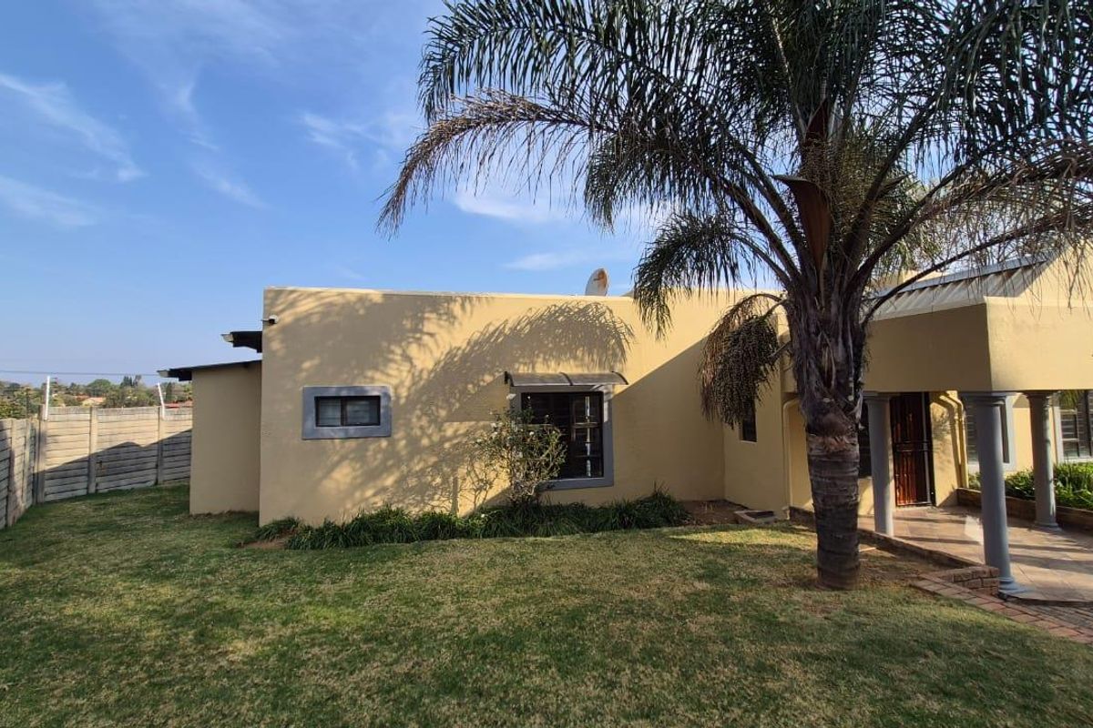 Rear view of the house featuring a covered patio with concrete columns, a paved walkway, and a well-maintained lawn enclosed by a boundary wall.
