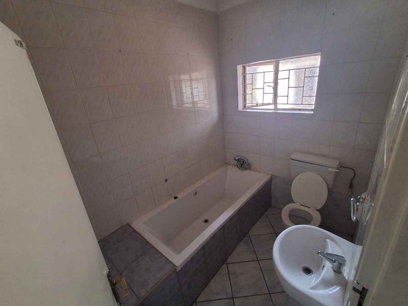 A functional bathroom featuring a built-in bathtub, pedestal basin, and toilet, finished with ceramic wall and floor tiles. Requires cosmetic updates.