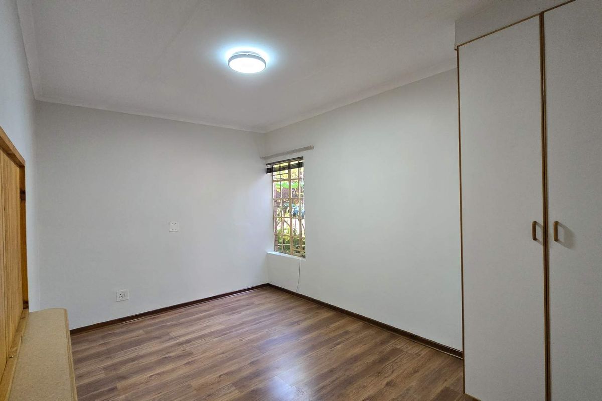 A bright, empty bedroom featuring laminate flooring, a built-in wardrobe, and a window with security bars.