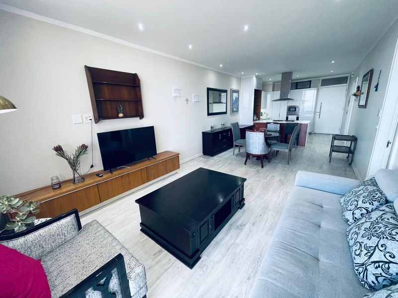 Spacious open-plan living and dining area featuring modern laminate flooring, recessed lighting, and a contemporary kitchen with a central island and built-in appliances.