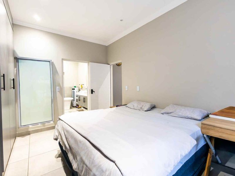 A well-maintained bedroom featuring neutral tones, tiled flooring, ample built-in cupboard space, and direct access to an en-suite bathroom.
