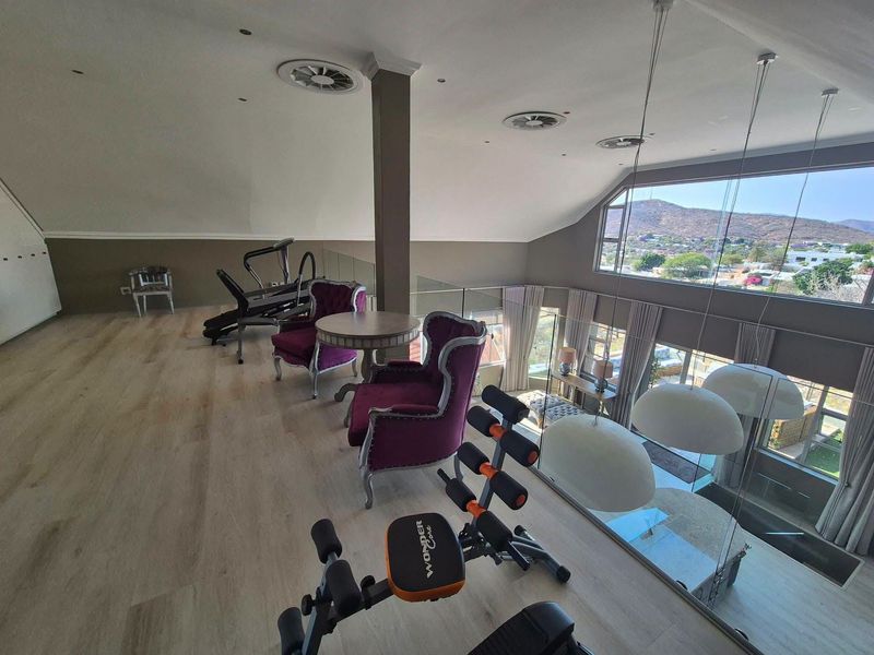 Spacious mezzanine gym area featuring modern laminate flooring, a glass balustrade overlooking the lower level, and large windows with scenic mountain views.