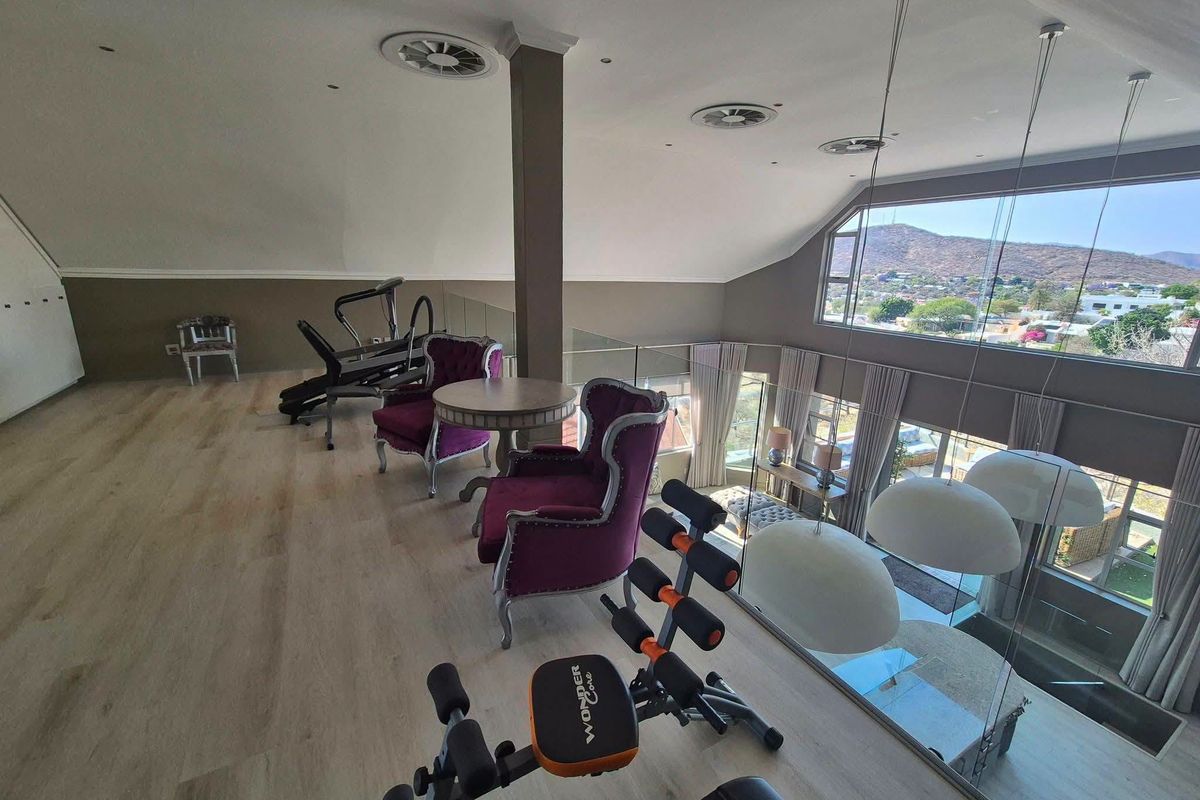 Spacious mezzanine gym area featuring modern laminate flooring, a glass balustrade overlooking the lower level, and large windows with scenic mountain views.
