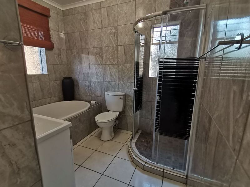 A functional bathroom featuring a corner shower enclosure, built-in bathtub, toilet, and vanity basin with full-height wall tiling.