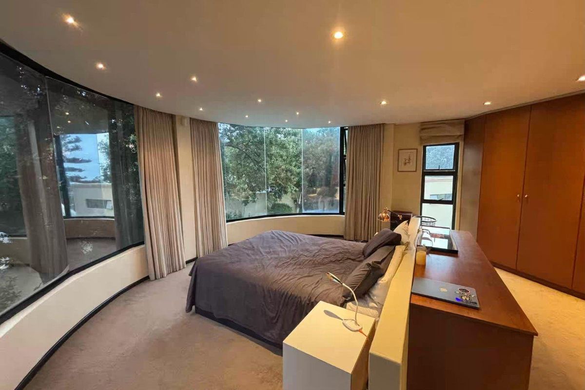 Spacious bedroom featuring a curved floor-to-ceiling window, recessed downlighting, and built-in wooden cabinetry.